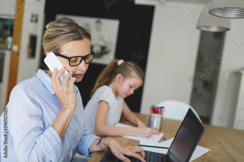 pretty young business woman works from home doing homeoffice  and her daughter has homeschooling during corona crisis photo