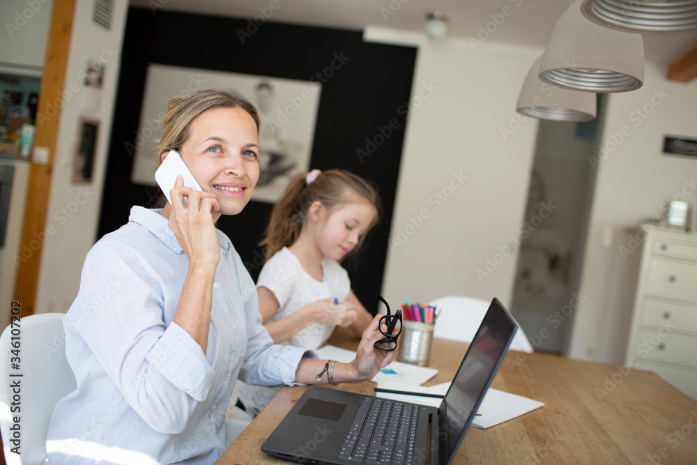 pretty young business woman works from home doing homeoffice and her daughter has homeschooling during corona crisis pretty young business woman works from home doing homeoffice and her daughter has homeschooling during corona crisis