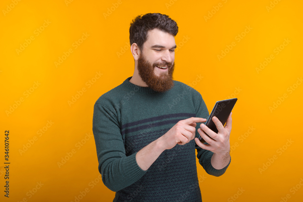 Calm smiling bearded man is using his tablet over yellow background. Calm smiling bearded man is using his tablet over yellow background.