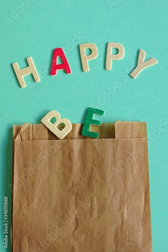 be happy word written in wooden letters coming out of a paper bag on a colored cardboard