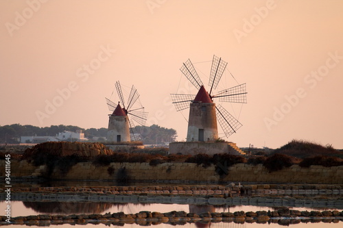evocative image of pair of windmills in a salt pan at sunset