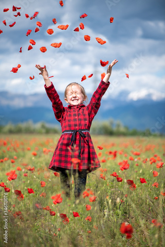 Five-year girl throws poppy petals in a field with poppies on a background of alpine mountains and blue clouds, vertical position