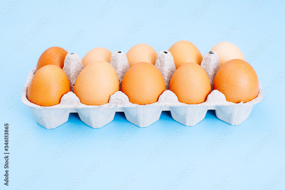 Overhead view of fresh brown chicken eggs in open egg carton box on blue background. Top view with copy space.