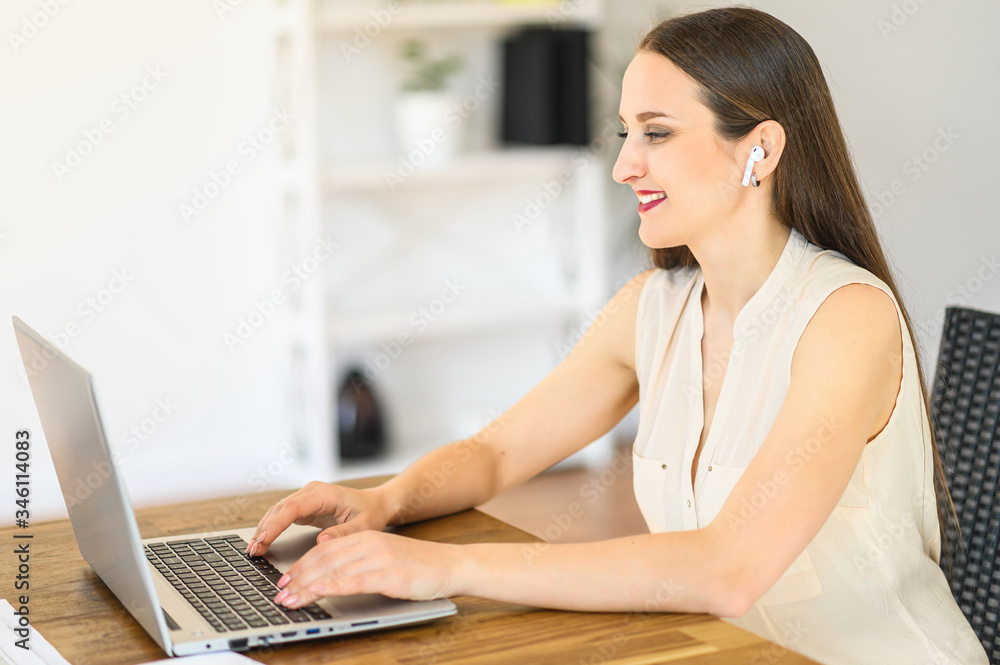 Close up a young attractive woman with airpods is using laptop for work in home office. Side view Close up a young attractive woman with airpods is using laptop for work in home office. Side view