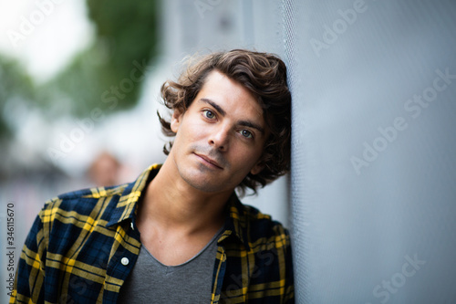 Close up handsome young man leaning against gray wall staring