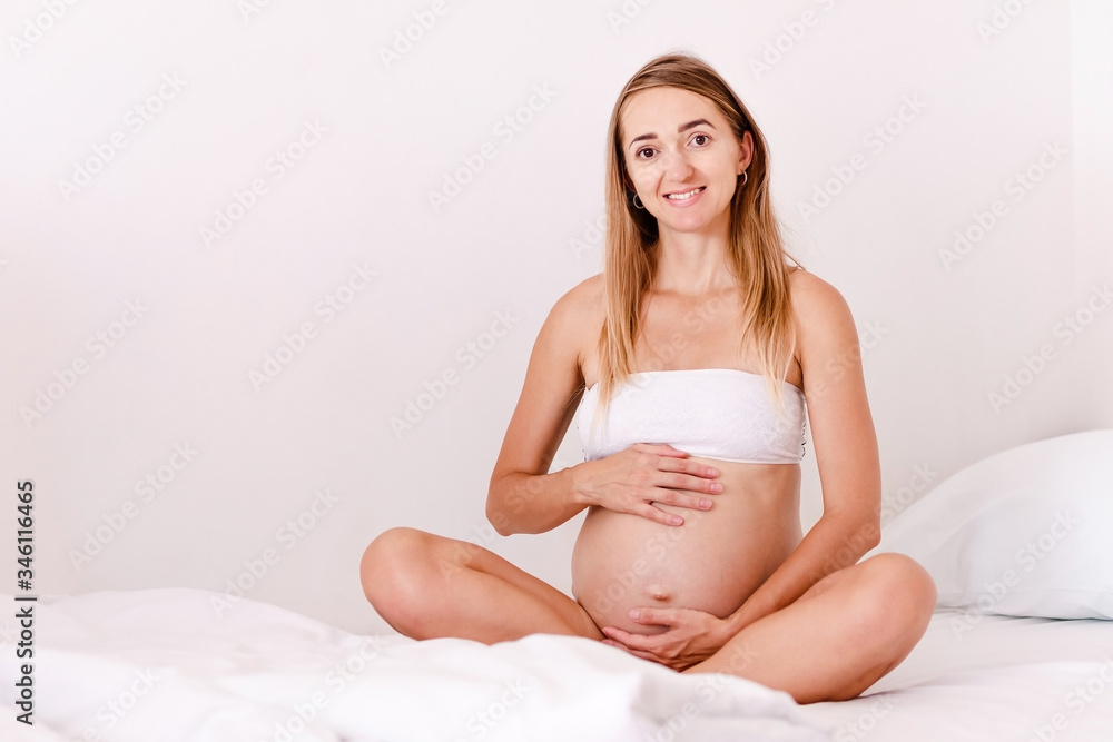 Smiling pregnant woman sits on the bed Smiling pregnant woman sits on the bed