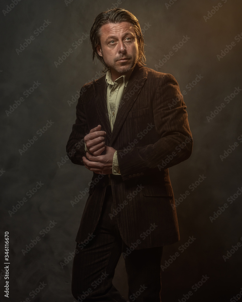Fashionable middle aged man in dark brown suit in front of grey wall. Low key studio shot. Fashionable middle aged man in dark brown suit in front of grey wall. Low key studio shot.