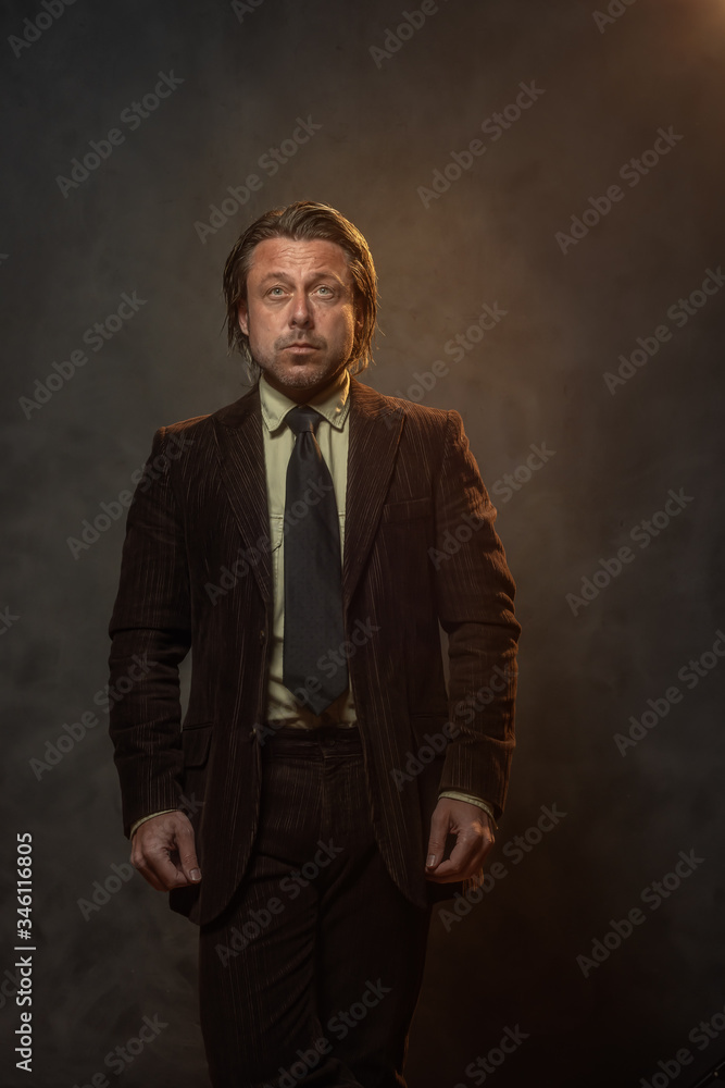 Cool middle aged businessman in dark brown suit and black tie in front of grey wall. Low key studio shot. Cool middle aged businessman in dark brown suit and black tie in front of grey wall. Low key studio shot.