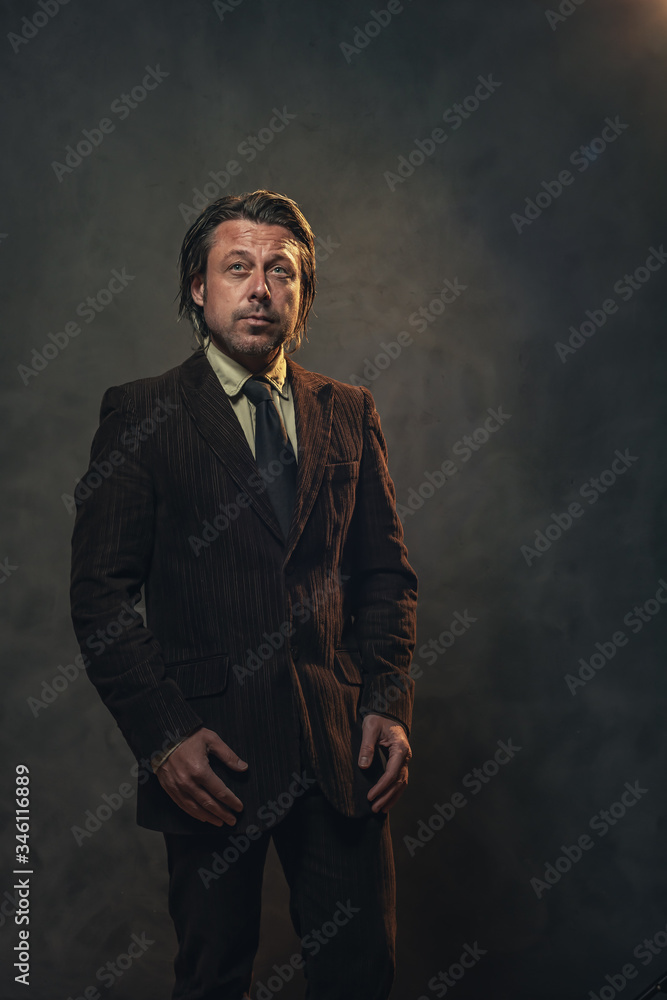 Cool middle aged businessman in dark brown suit and black tie in front of grey wall. Low key studio shot. Cool middle aged businessman in dark brown suit and black tie in front of grey wall. Low key studio shot.