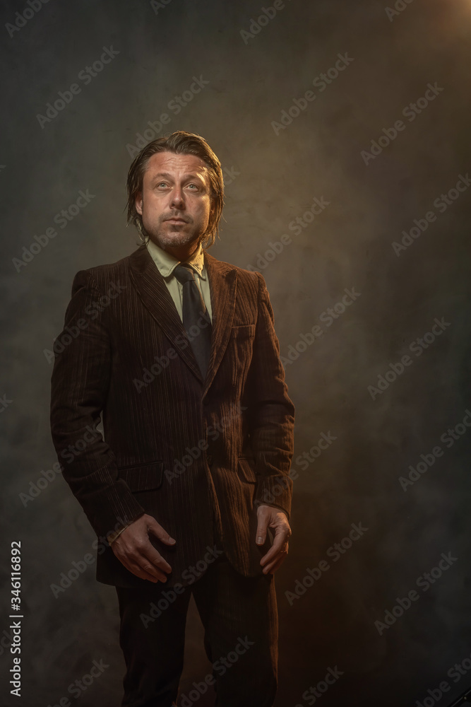 Cool middle aged businessman in dark brown suit and black tie in front of grey wall. Low key studio shot.