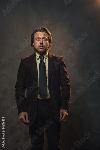 Cool middle aged businessman in dark brown suit and black tie in front of grey wall. Low key studio shot.