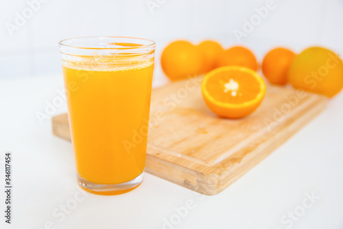 Foto Close-up of glass of orange juice in front of wooden board with two half of orange laying on it