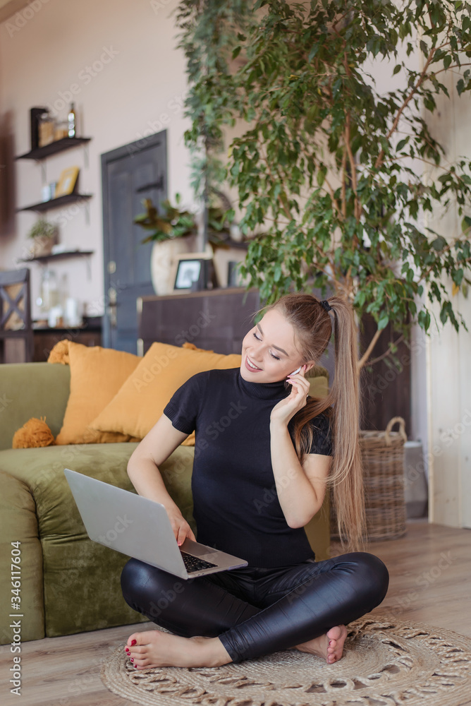 Obraz premium The girl talks to a colleague and friend in an online laptop program. A young woman with wireless headphones works at home with a computer. Online conference.