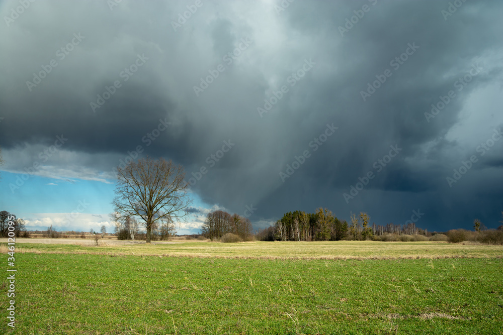 Dark cloud with snow and rain above green meadow