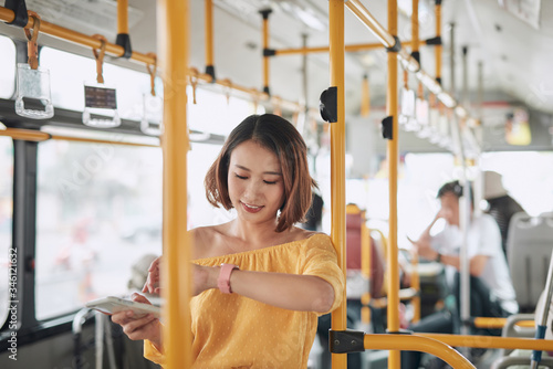 Beautiful asian woman standing in the bus checking time on her watch