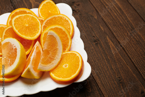 Fresh orange fruits sliced on a plate, dark wooden background - natural and healthy food.