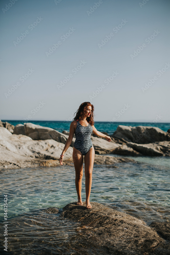 Young woman in bikini walking on rocks by the sea