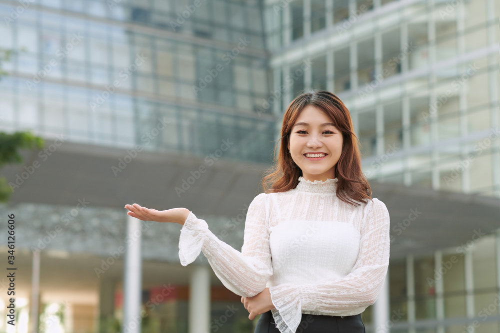 Beautiful asian woman with friendly smile has optimistic expression, shows something with her hand opened, standing outdoors. Youth and advertisement concept. Beautiful asian woman with friendly smile has optimistic expression, shows something with her hand opened, standing outdoors. Youth and advertisement concept.