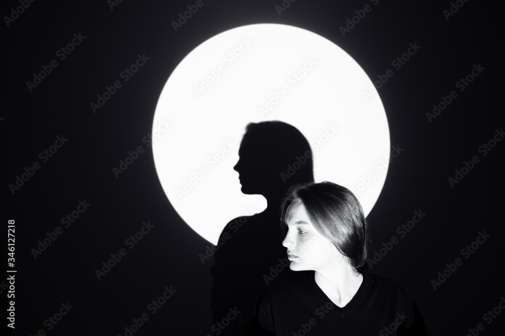Silhouette of a man against the moon. The girl stands and looks away. Its shadow is in the center of the circle. The rest of the image is dark. There is space for text and entries.