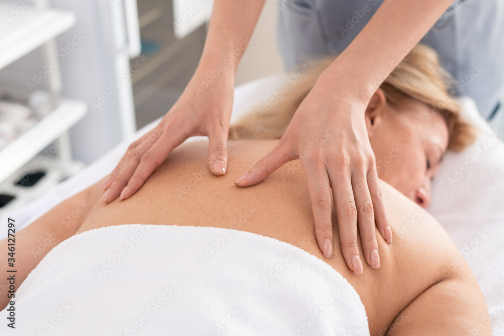 Close-up of unrecognizable therapist giving relaxing back massage to exhausted woman in spa salon
