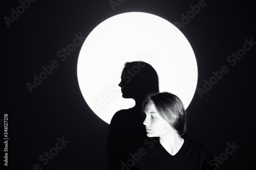 Silhouette of a man against the moon. The girl stands and looks away. Its shadow is in the center of the circle. The rest of the image is dark. There is space for text and entries.