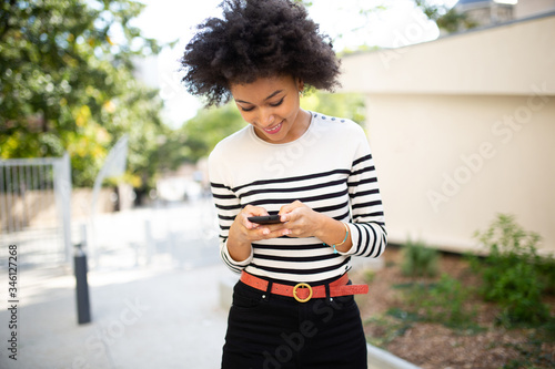 smiling young black woman looking at mobile phone outside