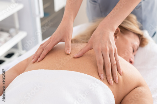 Close-up of unrecognizable therapist giving relaxing back massage to exhausted woman in spa salon