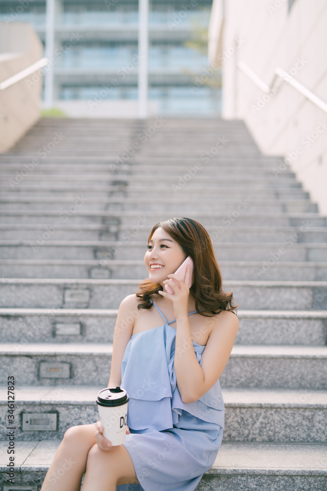 Cheerful young Asian girl talking on phone while sitting at outdoor stair. Lifestyle of urban girl. Cheerful young Asian girl talking on phone while sitting at outdoor stair. Lifestyle of urban girl.