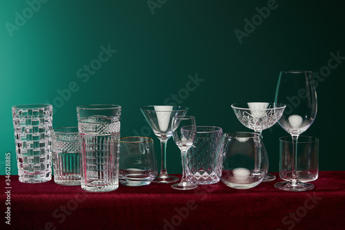 set of glasses: old fashioned glass, cocktail glass, champagne flute, shot glass, highball glass, collins glass, brandy glass, cognac balloon and collins glass on green background