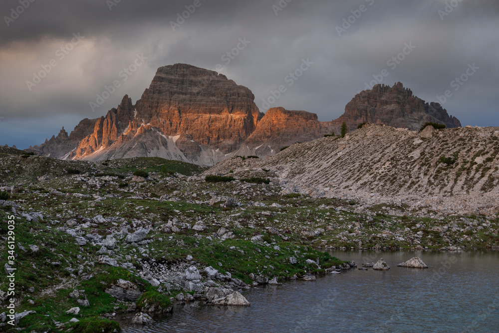 Mountain landscape in the European Dolomite Alps underneath the Three Peaks with alpenglow and lake during sunset, heavy clouds in the sky, South Tyrol Italy.