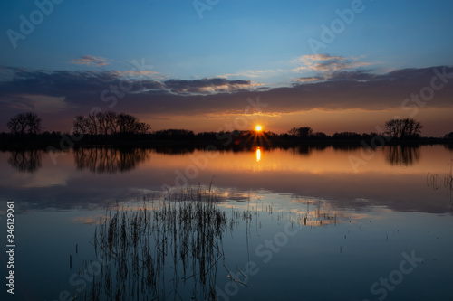 Sunset over a calm lake with reeds, the evening cloud reflecting in the water