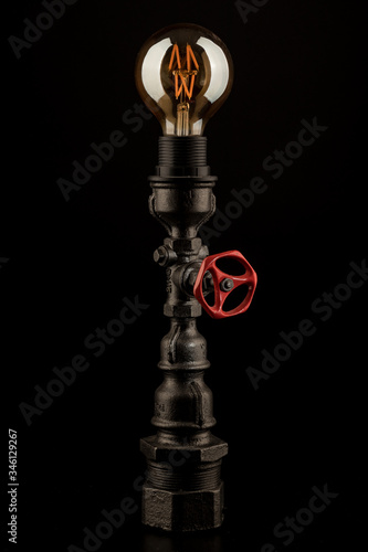 Vintage lamp made from steel water pipe fittings with filament bulb and valve switch, on black background
