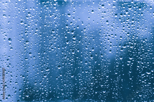 rain drops on a blue window glass transparent surface. water droplets on window shield in a rainy days in autumn spring summer winter in night. stormy weather. loneliness sad depression. rainy season. © Natallia