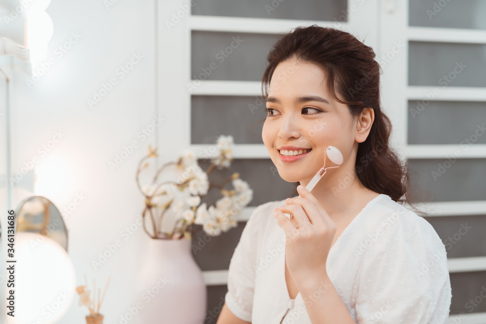 Woman using jade facial roller for face massage at home. Woman using jade facial roller for face massage at home.