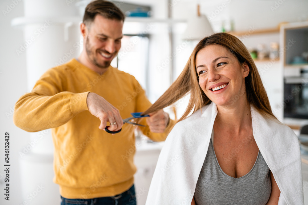 Fototapeta premium Couple having hair cut at home during quarantine coronavirus pandemic, online hairdressing on tablet