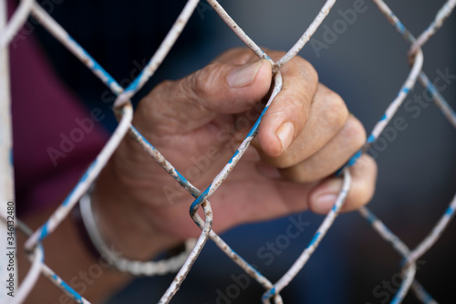 the hand of a man holding on to a cyclone wire fence. Possibly he is incarcerated or locked out photo