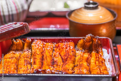 Close-up on fillets of japanese unagi eel  grilled in a kabayaki style topped on steamed white rice in a lackered jubako food box. photo