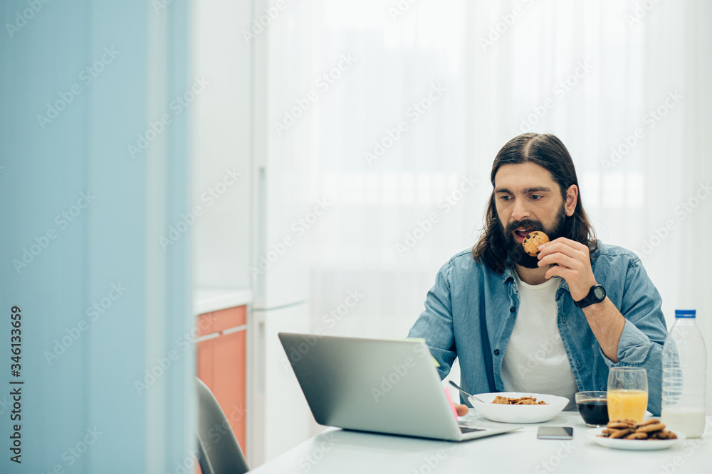 Hungry man eating breakfast and looking at the laptop screen Hungry man eating breakfast and looking at the laptop screen
