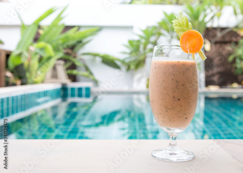 Mixed fruit and vegetables smoothie drink on swimming pool edge over blurred garden background, outdoor day light, healthy life style, diet drink