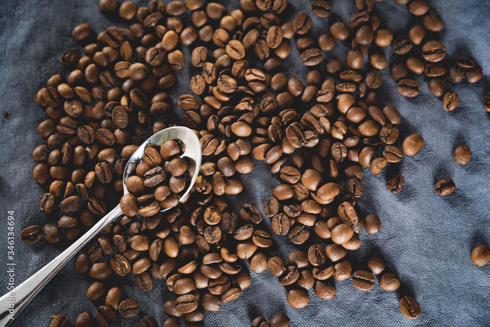 Dark roast coffee beans scattered on dark background with spoon. Coffee texture, flat lay Dark roast coffee beans scattered on dark background with spoon. Coffee texture, flat lay