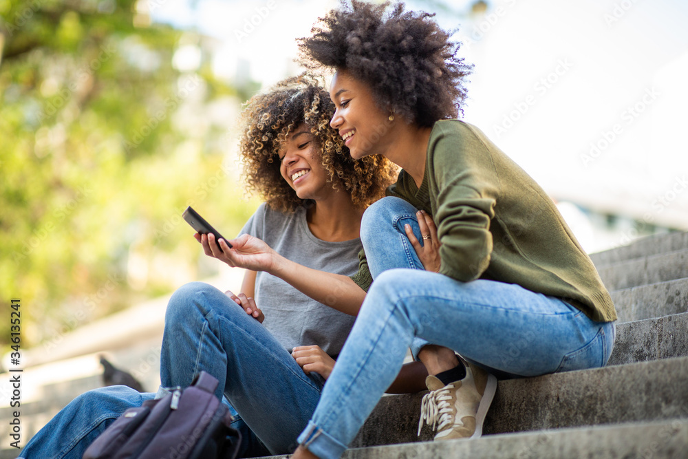 Side of two young african american women sitting on steps outside looking at cellphone Side of two young african american women sitting on steps outside looking at cellphone