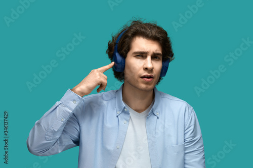 Can't hear you. Portrait of a young beautiful man wearing white t-shirt and blue shirt points a finger at the headphones on his head