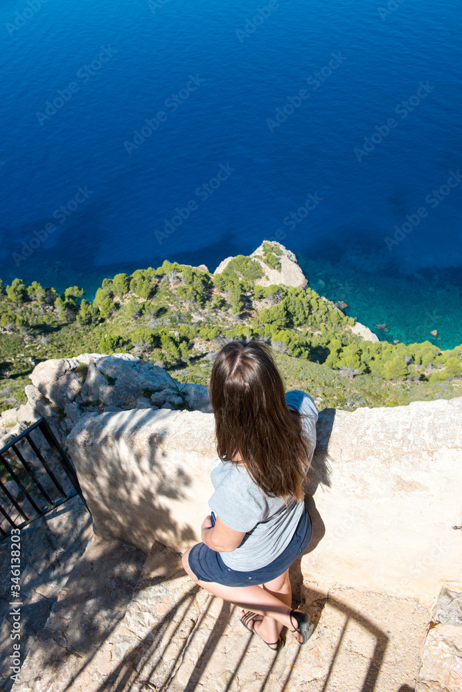 Back view of a young tourist woman looking at the ocean from the cliff Back view of a young tourist woman looking at the ocean from the cliff