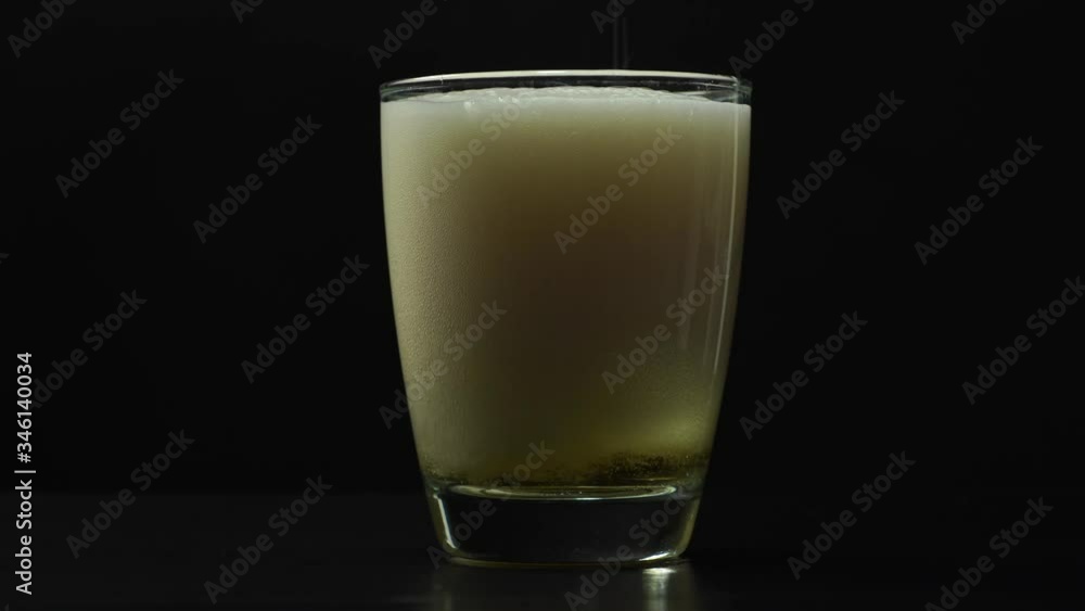 Pouring fresh and cold craft beer into a glass with white foam on top on black background. Flowing foamy wheat or lager beer on dark background Pouring fresh and cold craft beer into a glass with white foam on top on black background. Flowing foamy wheat or lager beer on dark background