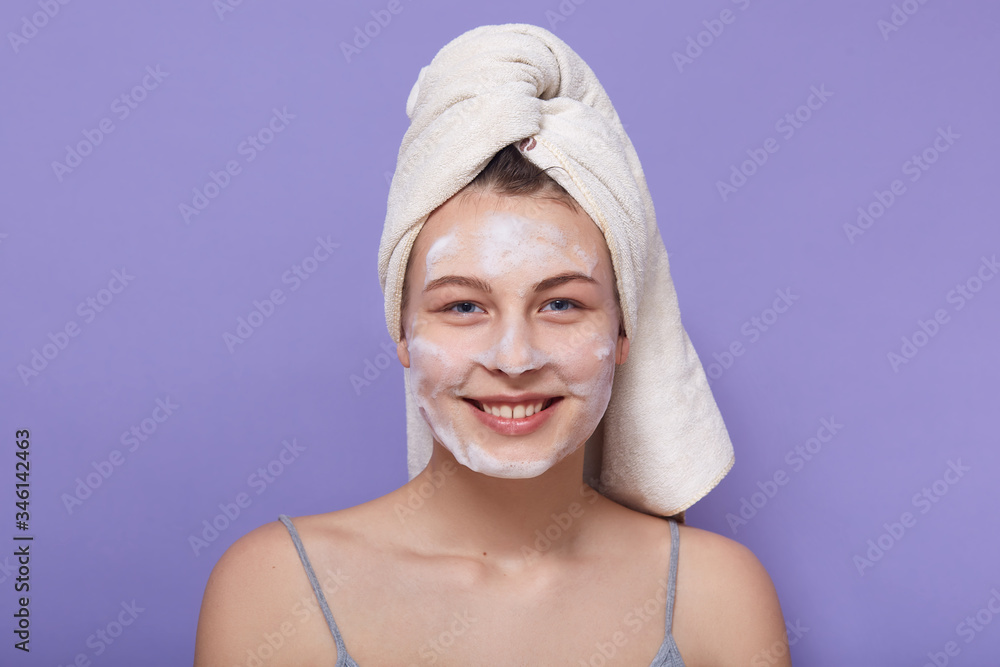 Closeup portrait of smiling happy female posing wrapped in white towel, looking directly at camera, posing isolated over lilac background. Skincare, cosmetology, morning procedures, spa concept. Closeup portrait of smiling happy female posing wrapped in white towel, looking directly at camera, posing isolated over lilac background. Skincare, cosmetology, morning procedures, spa concept.