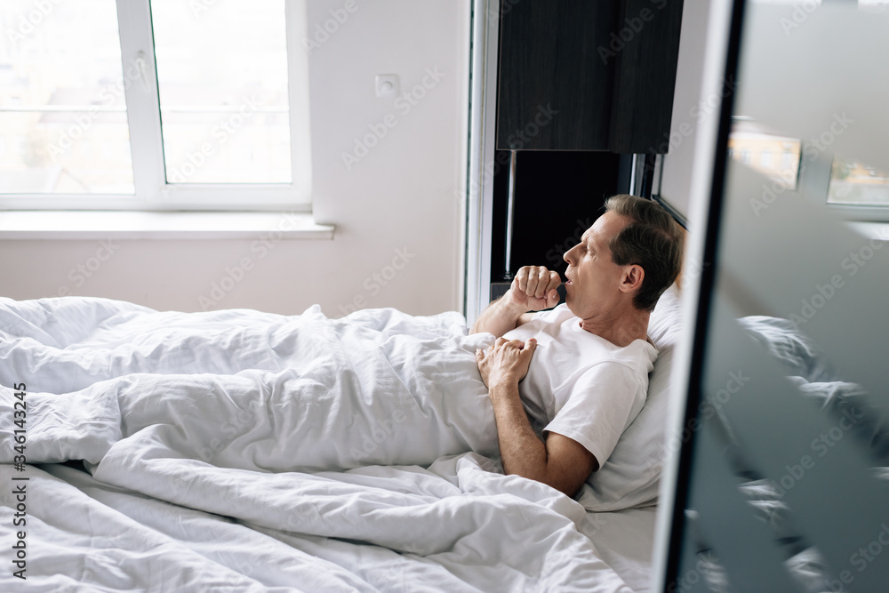 selective focus of diseased man coughing while lying on bed at home