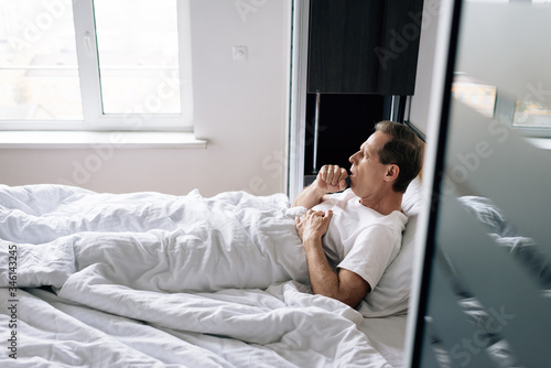 selective focus of diseased man coughing while lying on bed at home