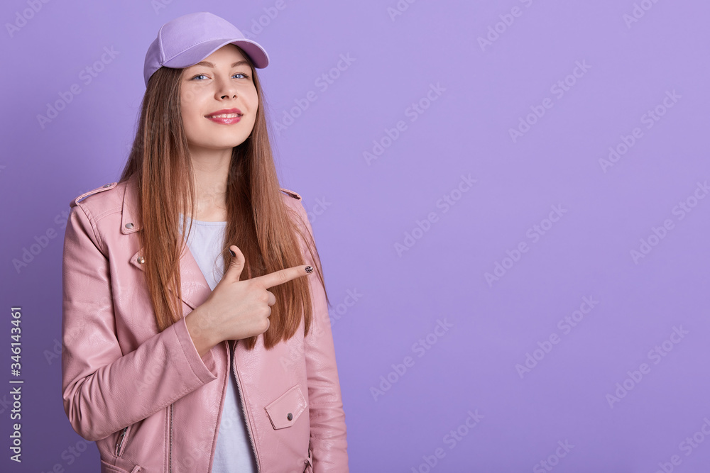 Portrait of charismatic stylish young female raising hand, making gesture, showing direction with forefinger, wearing t shirt, jacket and cap, looking directly at camera. Copyspace for advertisement. Portrait of charismatic stylish young female raising hand, making gesture, showing direction with forefinger, wearing t shirt, jacket and cap, looking directly at camera. Copyspace for advertisement.