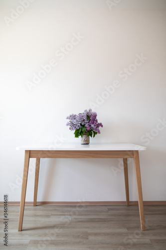 On a white table is a vase of lilac flowers