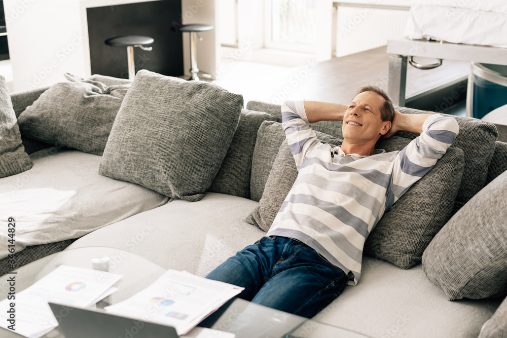cheerful man relaxing on sofa near charts and graphs on coffee table